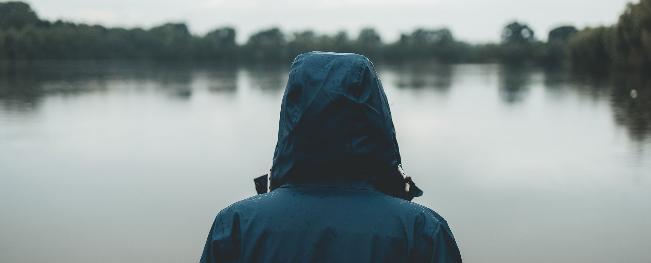 person in regenjacke schaut auf see