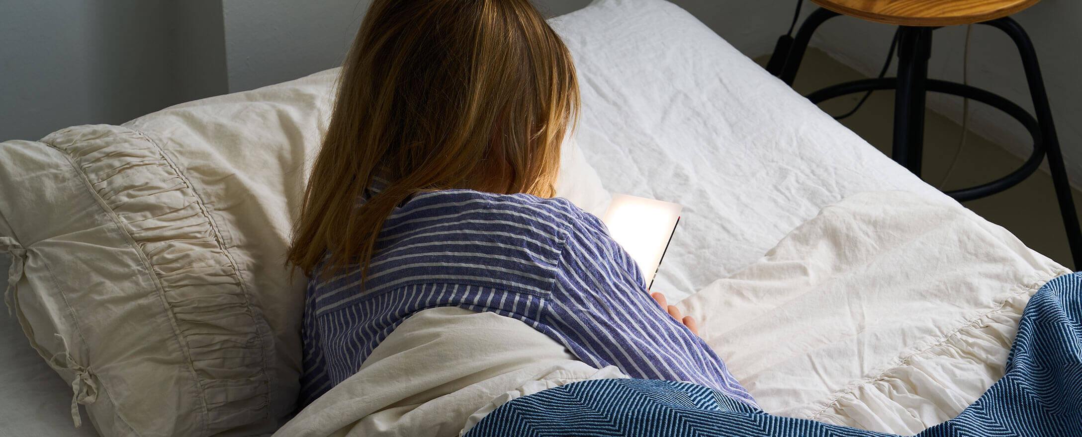 Frau liegt im Bett und schaut auf ihr Handy und es strahlt sie an 