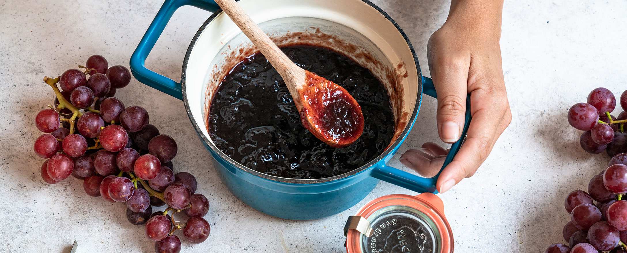 frau beim einkochen von marmelade mit weintrauben