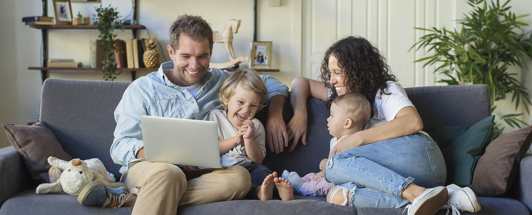 Familie sitzt und lacht gemeinsam auf Couch. 